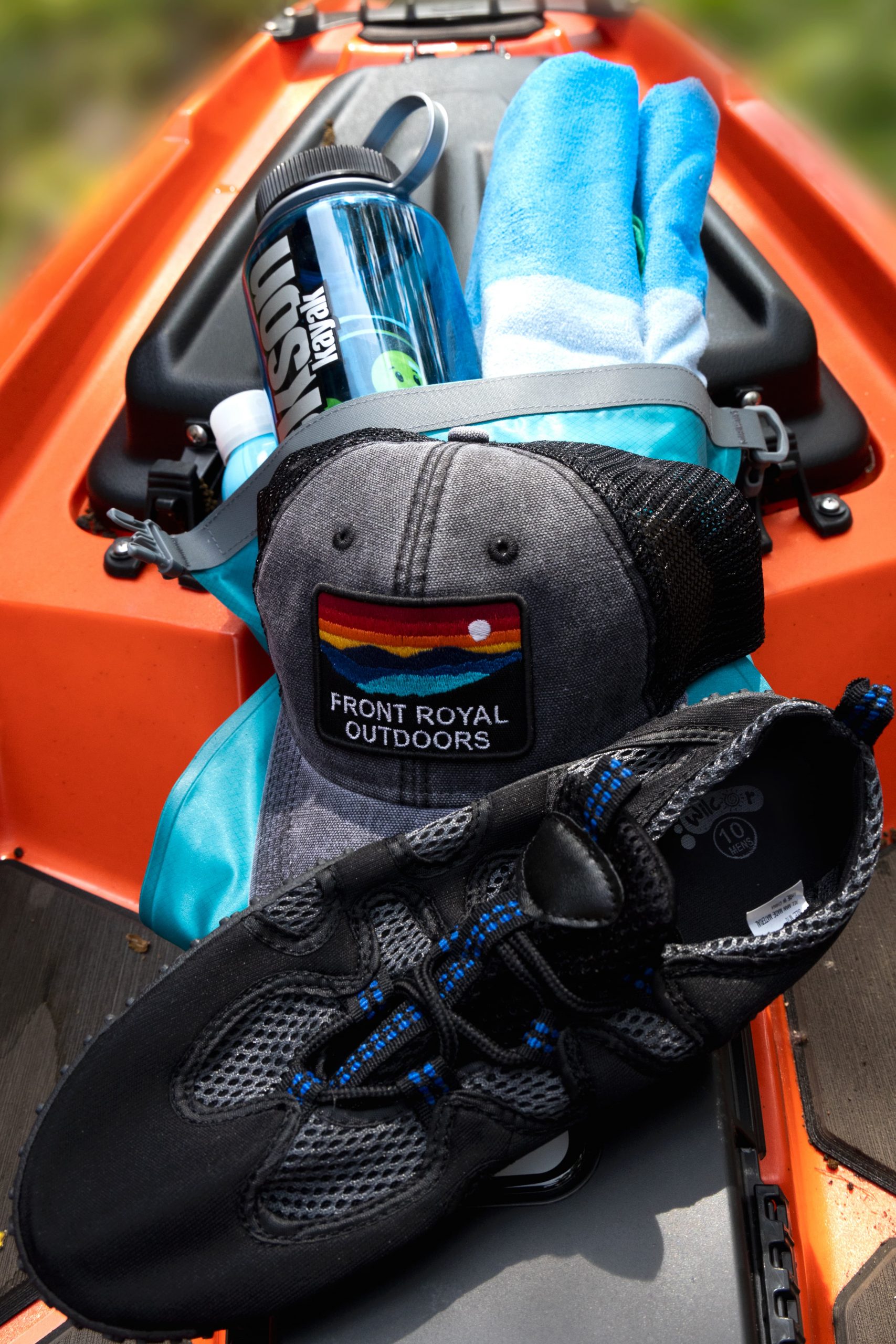 a baseball hat, water shoes, water bottle, and towel in an orange kayak