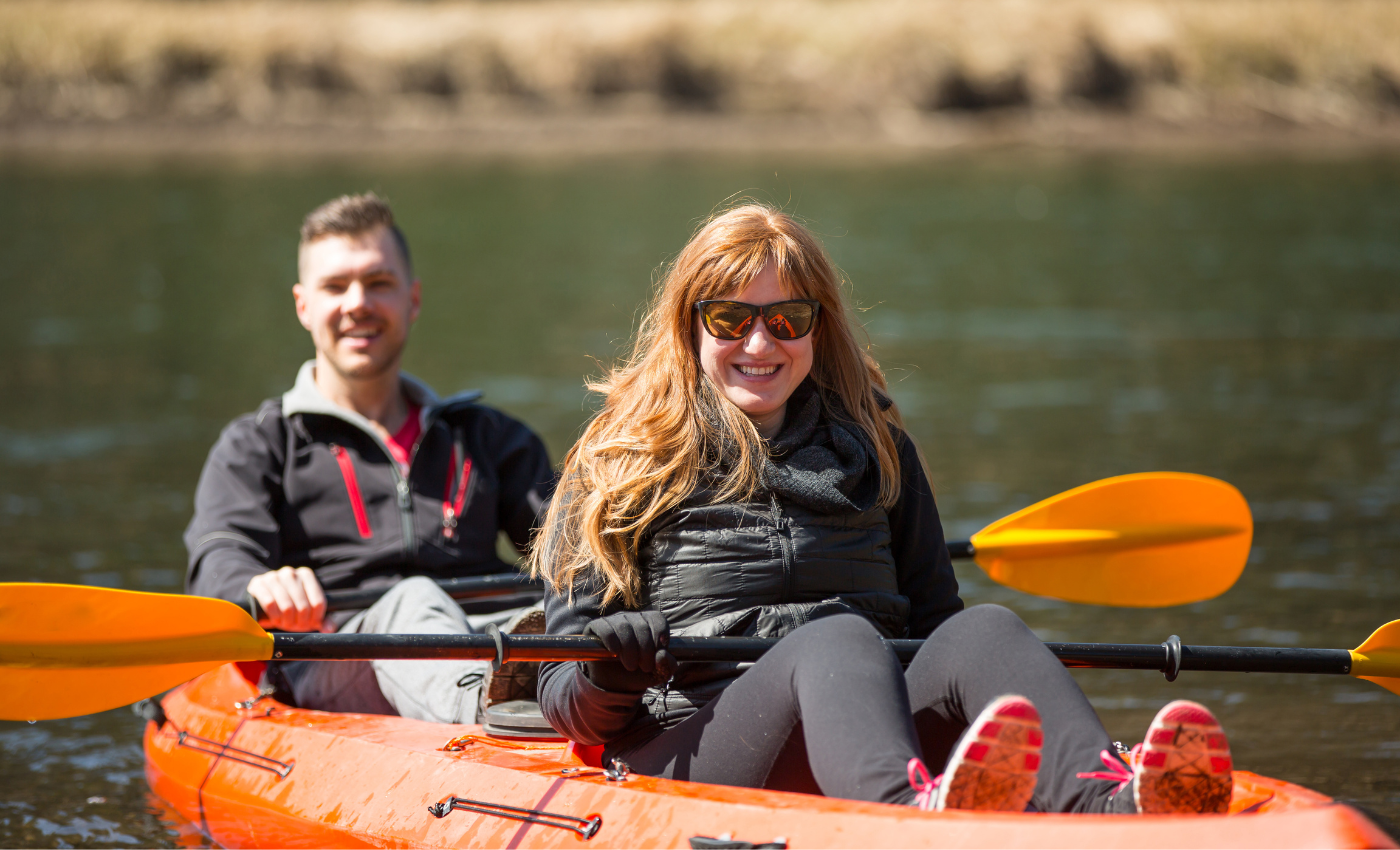 a man and woman paddle in an orange tandem kayak