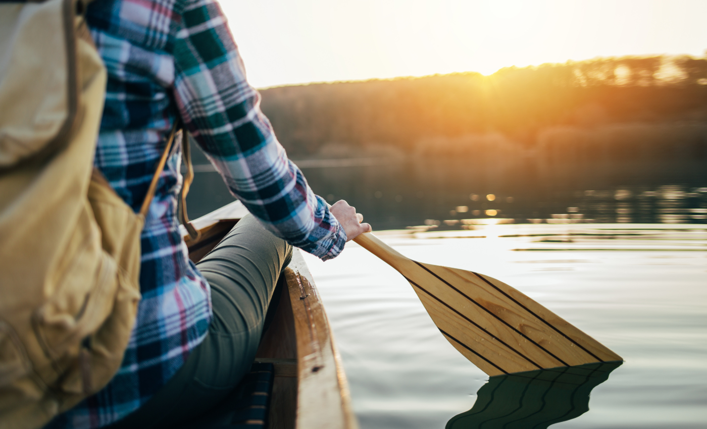 a paddler puts a paddle into flat water at sunset while canoeing