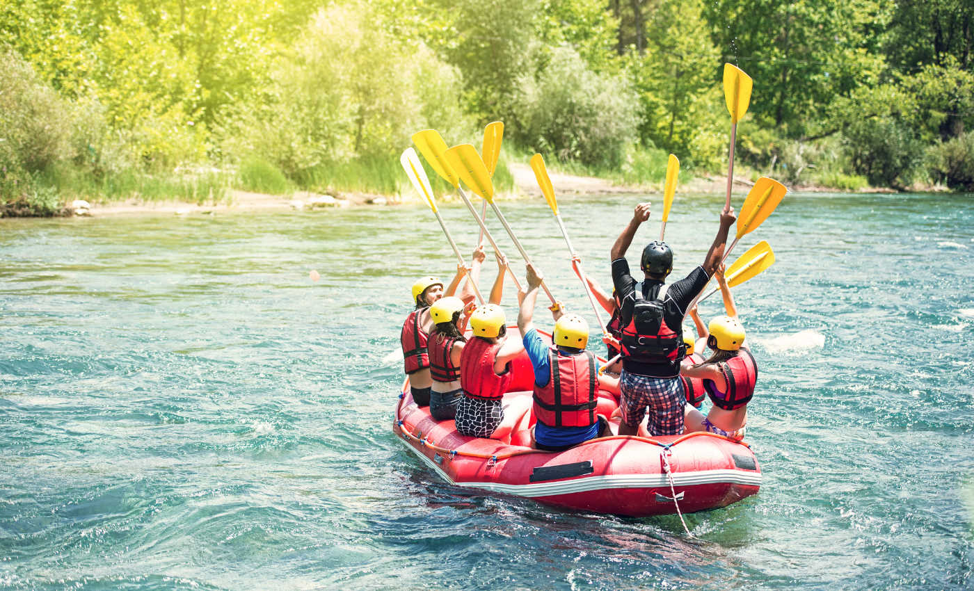 a red raft with several rafters raise their paddles in the air