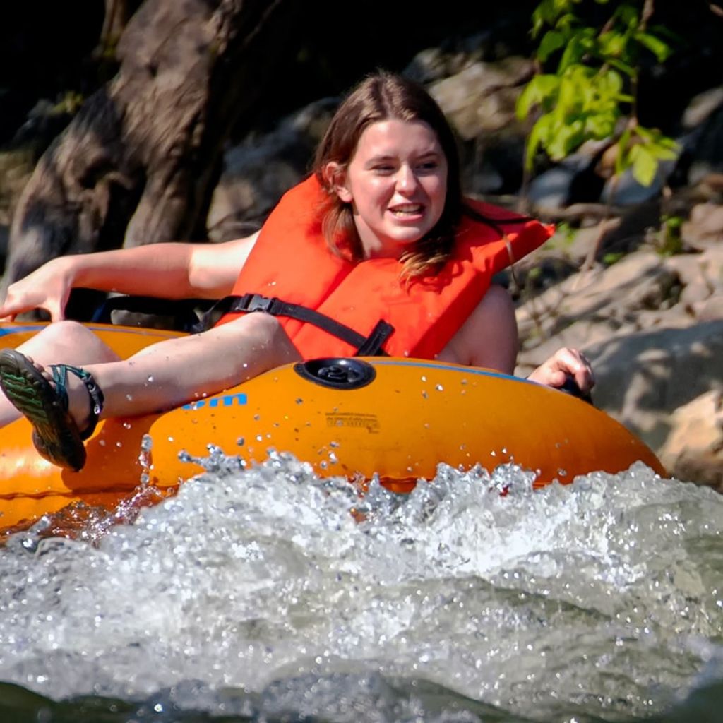 a girl floats down a river in an orange tube