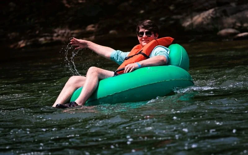 man is sitting on a green tube on the Shenandoah River
