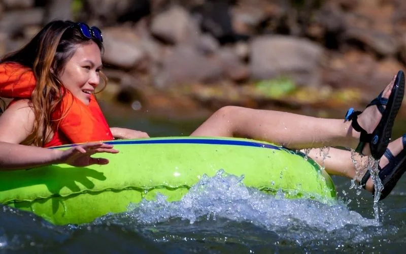 A woman floats down a river in a green river tube