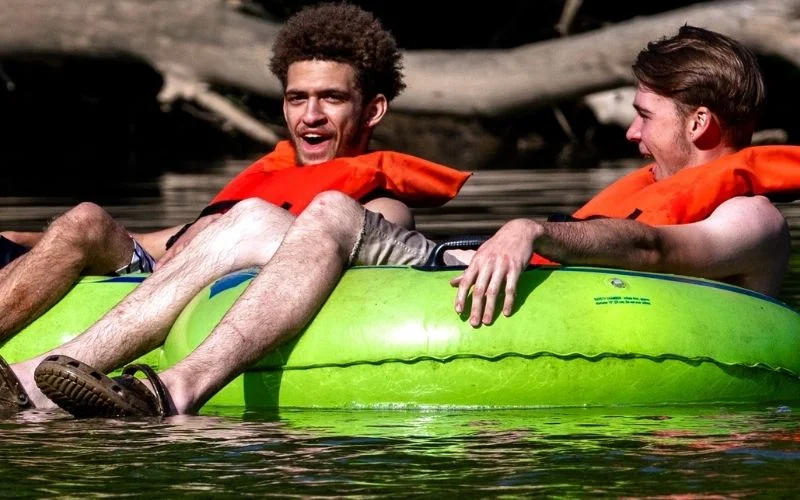 Two men laughing while floating down a river in tubes